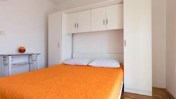 A bedroom with a bed, white wardrobe, and a small table with a lamp.