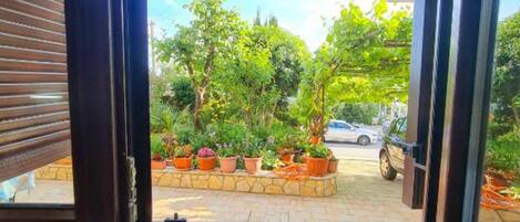 An open sliding glass door leading to a patio with potted plants and a parked car.