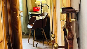 A hallway with a wooden door, a chair, a table with a lamp, and a towel rack.