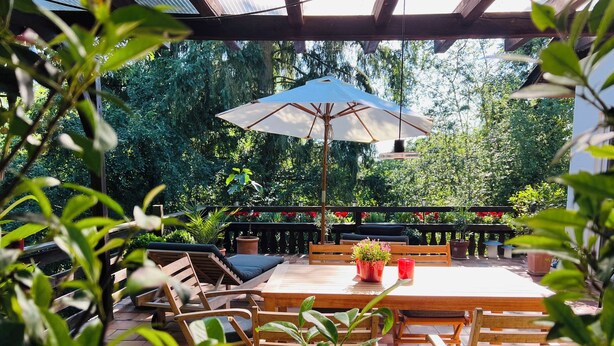 An outdoor patio with wooden furniture, a table, and a large umbrella.