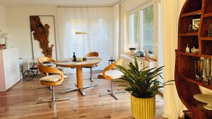A modern dining area with a round table, four chairs, a potted plant, and a wooden bookshelf.