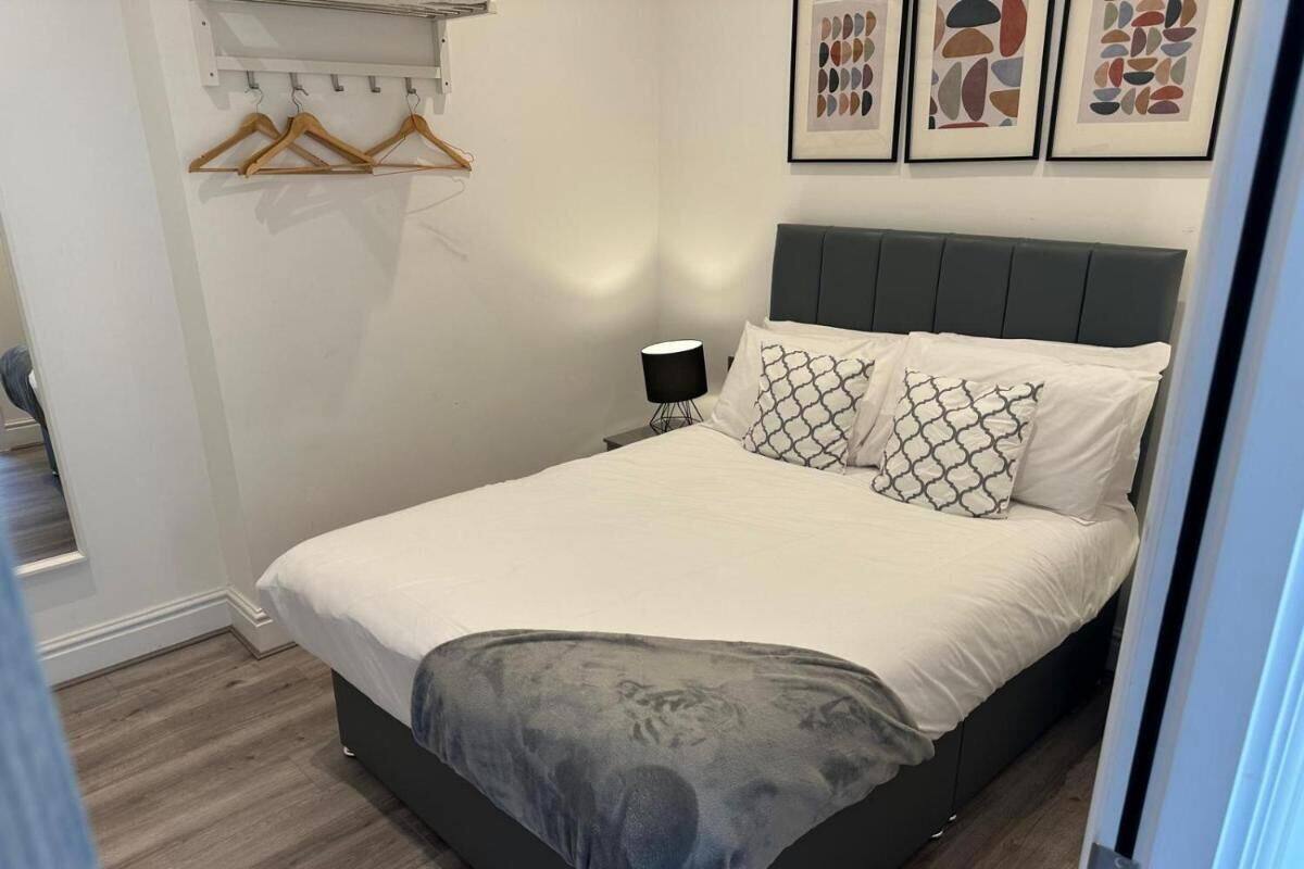 A bedroom with a bed, a bedside table, a lamp, and a wall-mounted coat rack.
