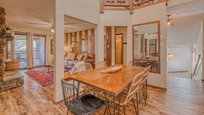 En rummelig spiseplads med et træbord og stole, en stenspir og udsigt over naturen gennem store skydedøre.