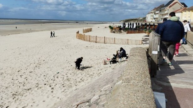 A beach with a wooden fence, a few people, and a building in the background.