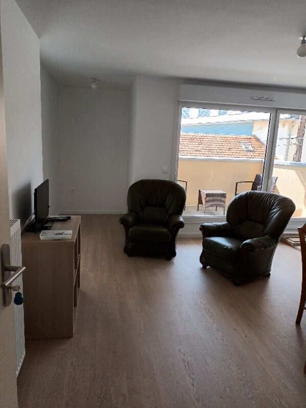 A spacious living room with two leather armchairs, a small table, and a radiator. A large window offers a view of the outside. - Modern, new apartment 200 meters from the sea in Fort Mahon (Fort-Mahon-Plage)