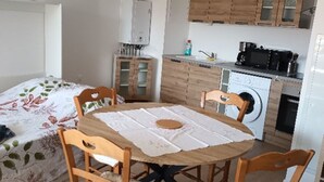A small, cozy kitchen with wooden cabinets, a washing machine, and a dining table with chairs.