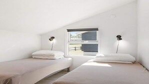 Une chambre avec deux lits simples, une fenêtre donnant sur une grange et deux lampes fixées au mur.