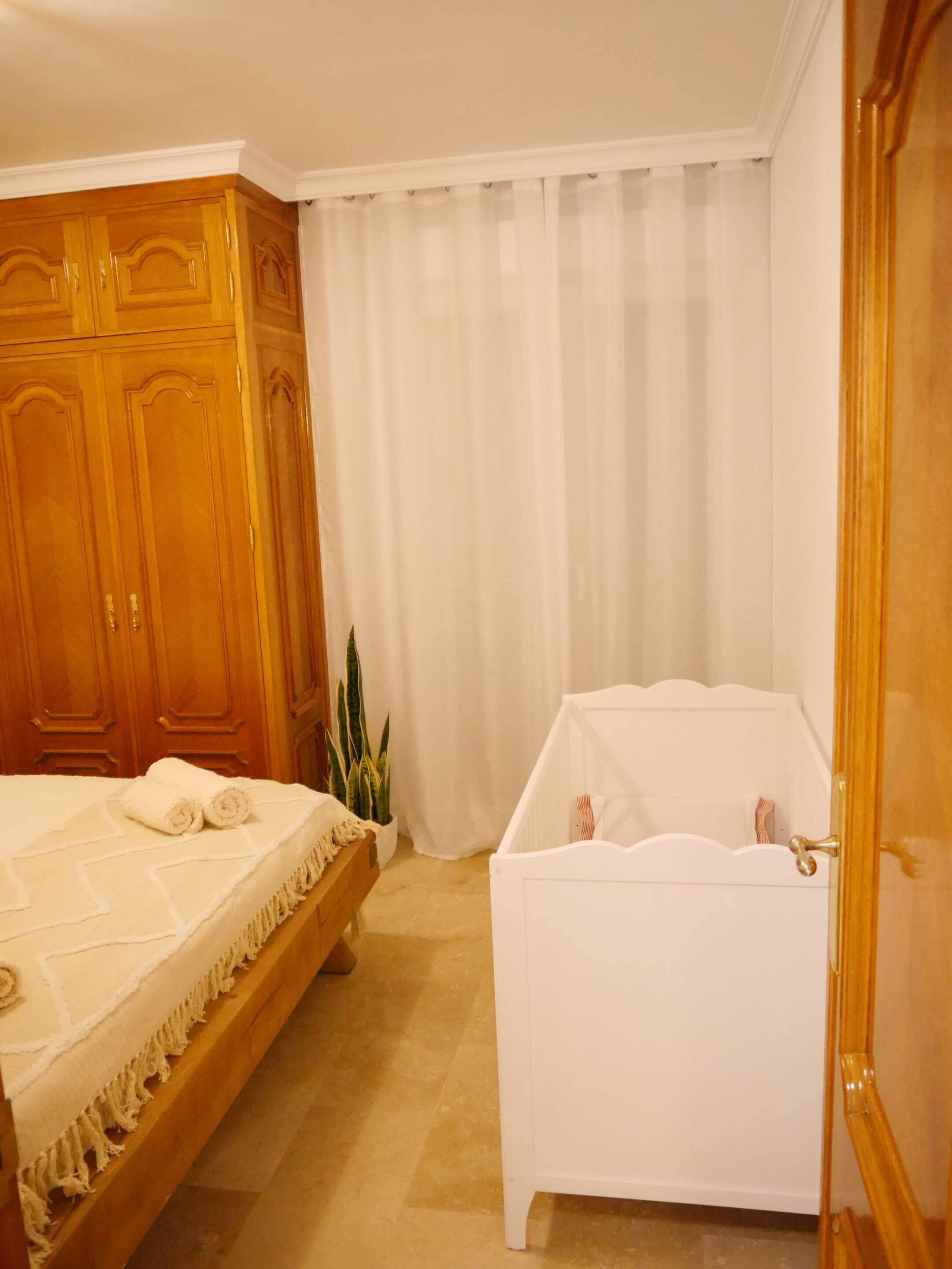 A bedroom with a bed, a white bathtub, wooden wardrobe, and a potted plant.