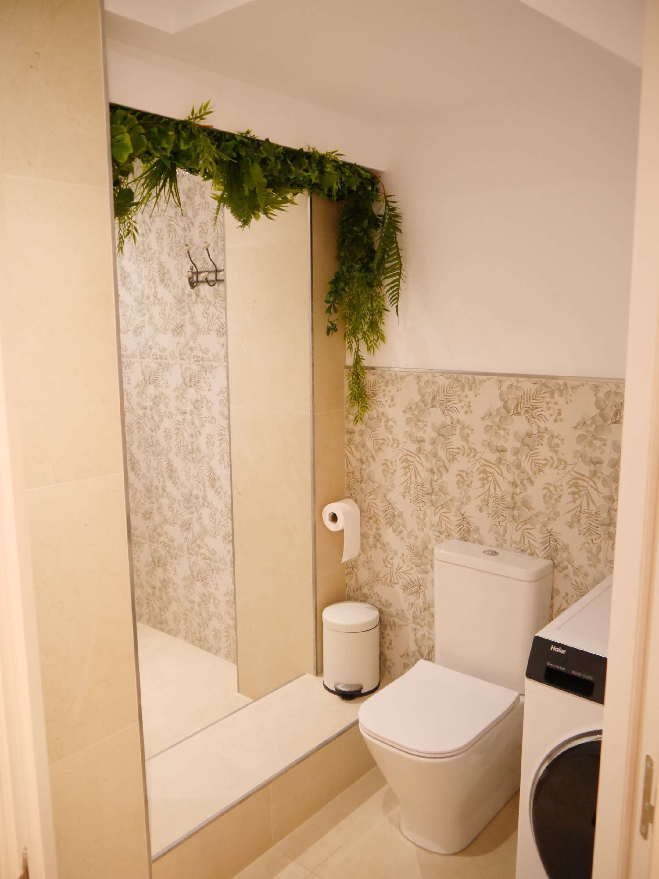 A bathroom with a toilet, a washing machine, and a shower area with a green plant decoration.