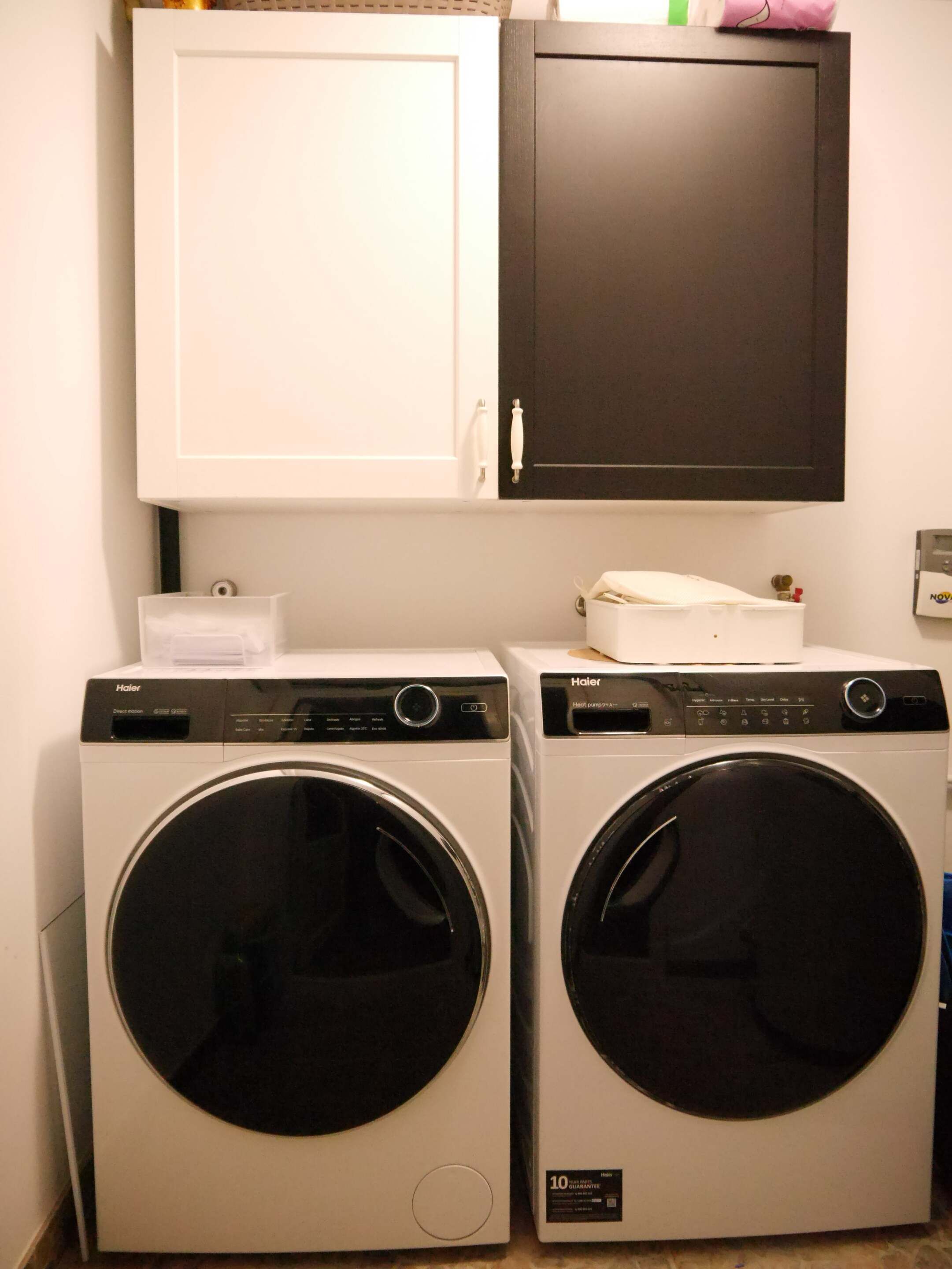 Deux machines à laver Haier à chargement frontal sont installées dans une buanderie, au-dessus desquelles se trouve un meuble blanc.
