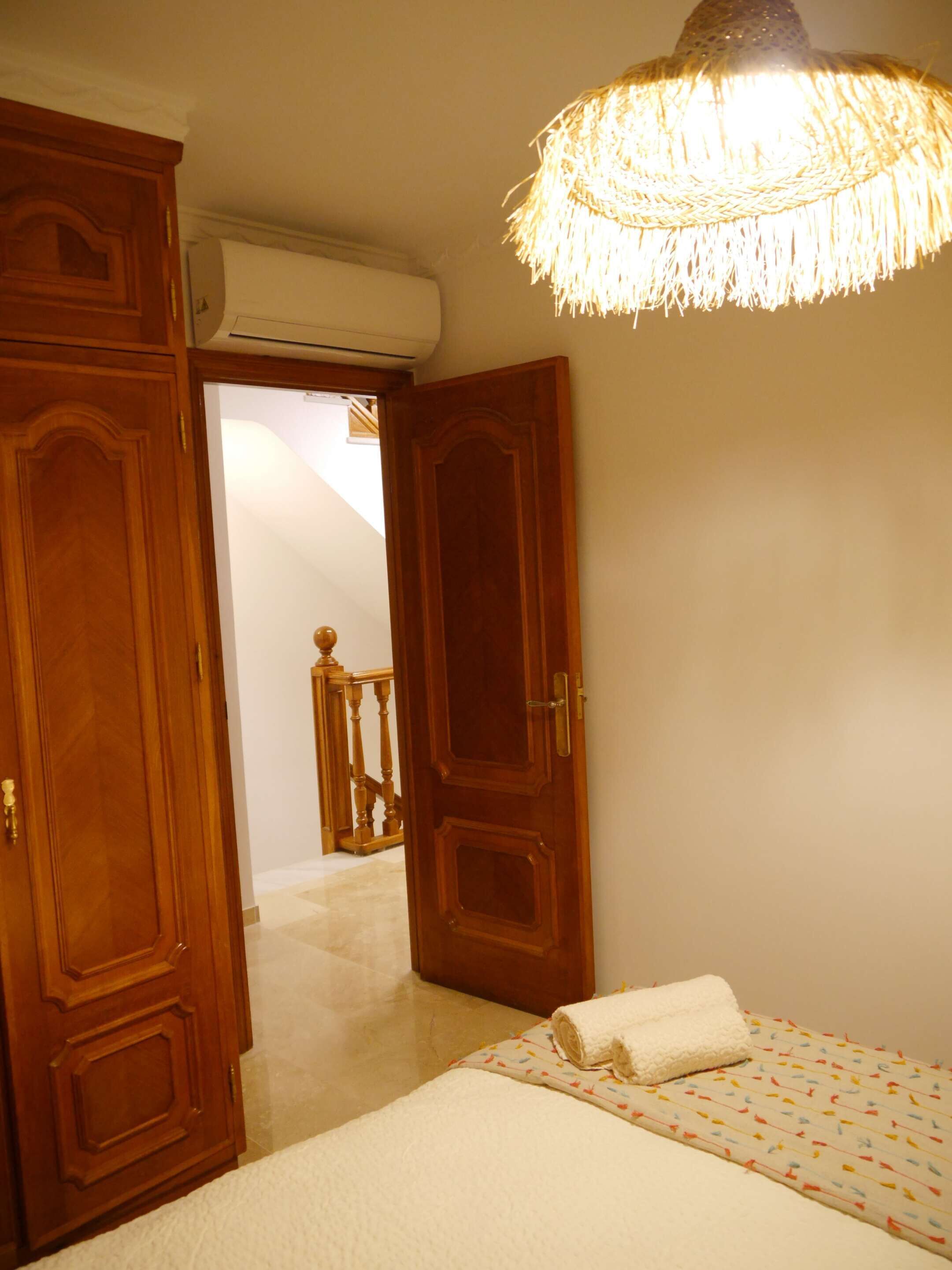 Un dormitorio con cama, armario de madera y lámpara colgante.