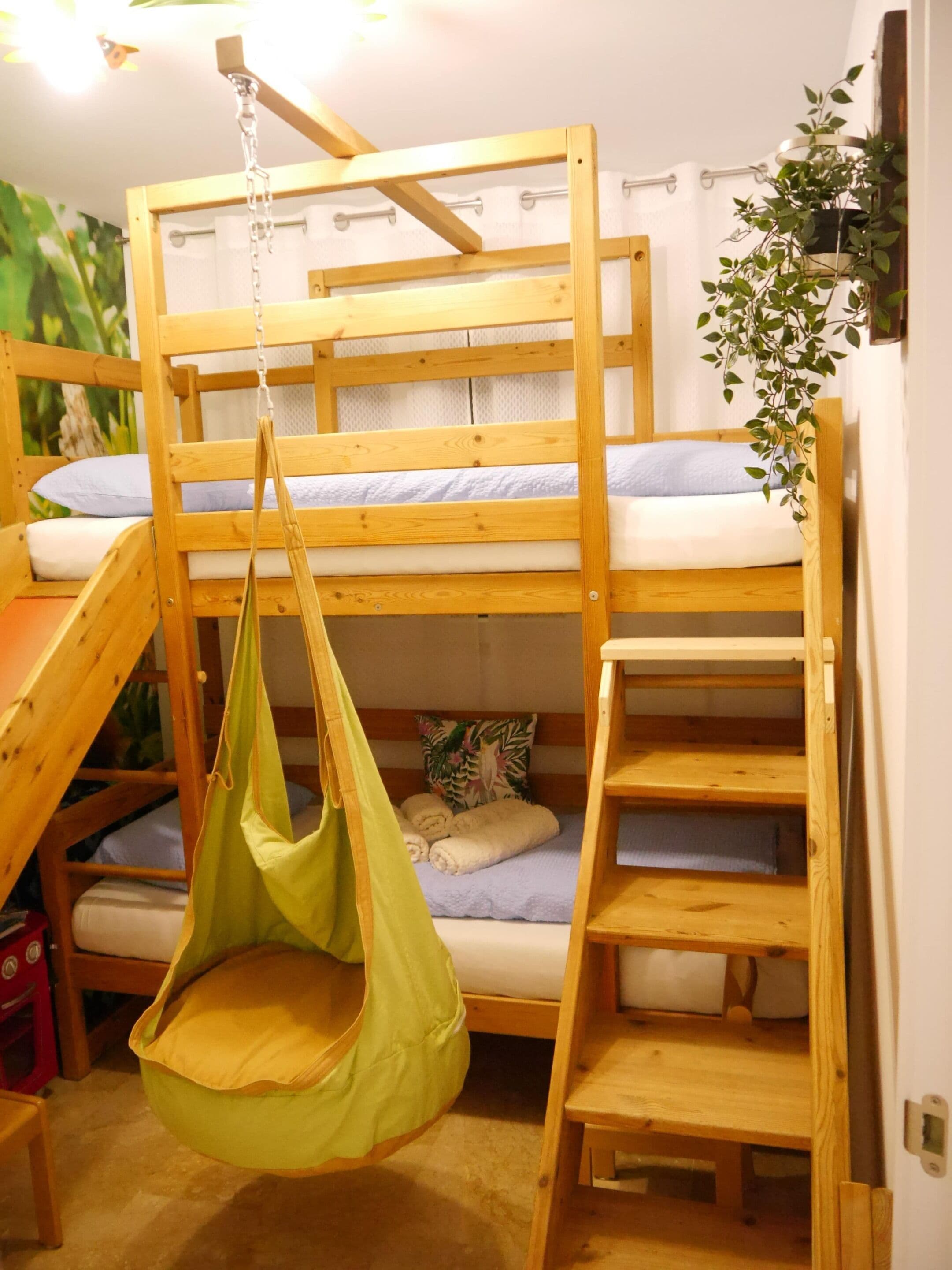 Ein Stockbett mit Hängekorbschaukel, Holzstufen und einer Pflanze.