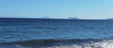 A coastal view with waves crashing onto the shore and a distant mountain range.