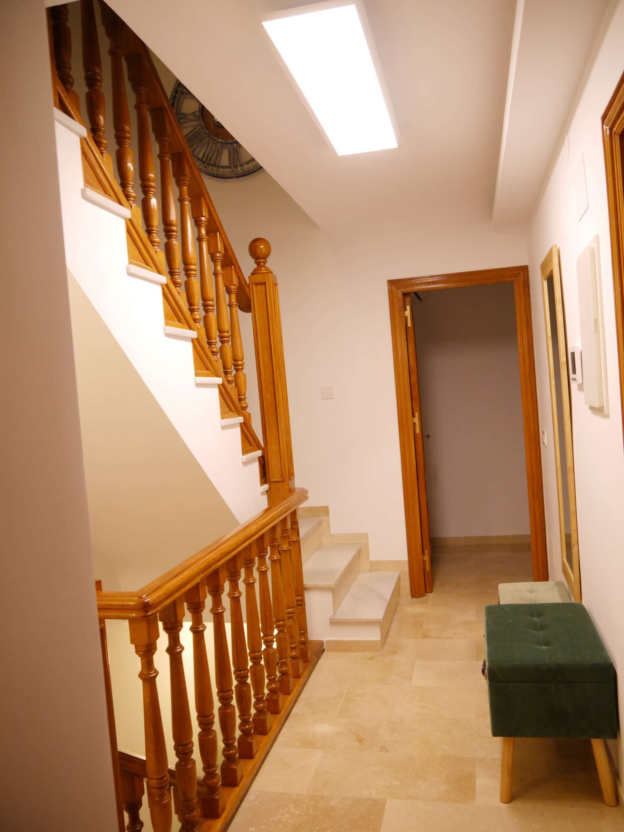 A staircase with wooden balusters leading to a landing, a bench, and a door at the end of a hallway.