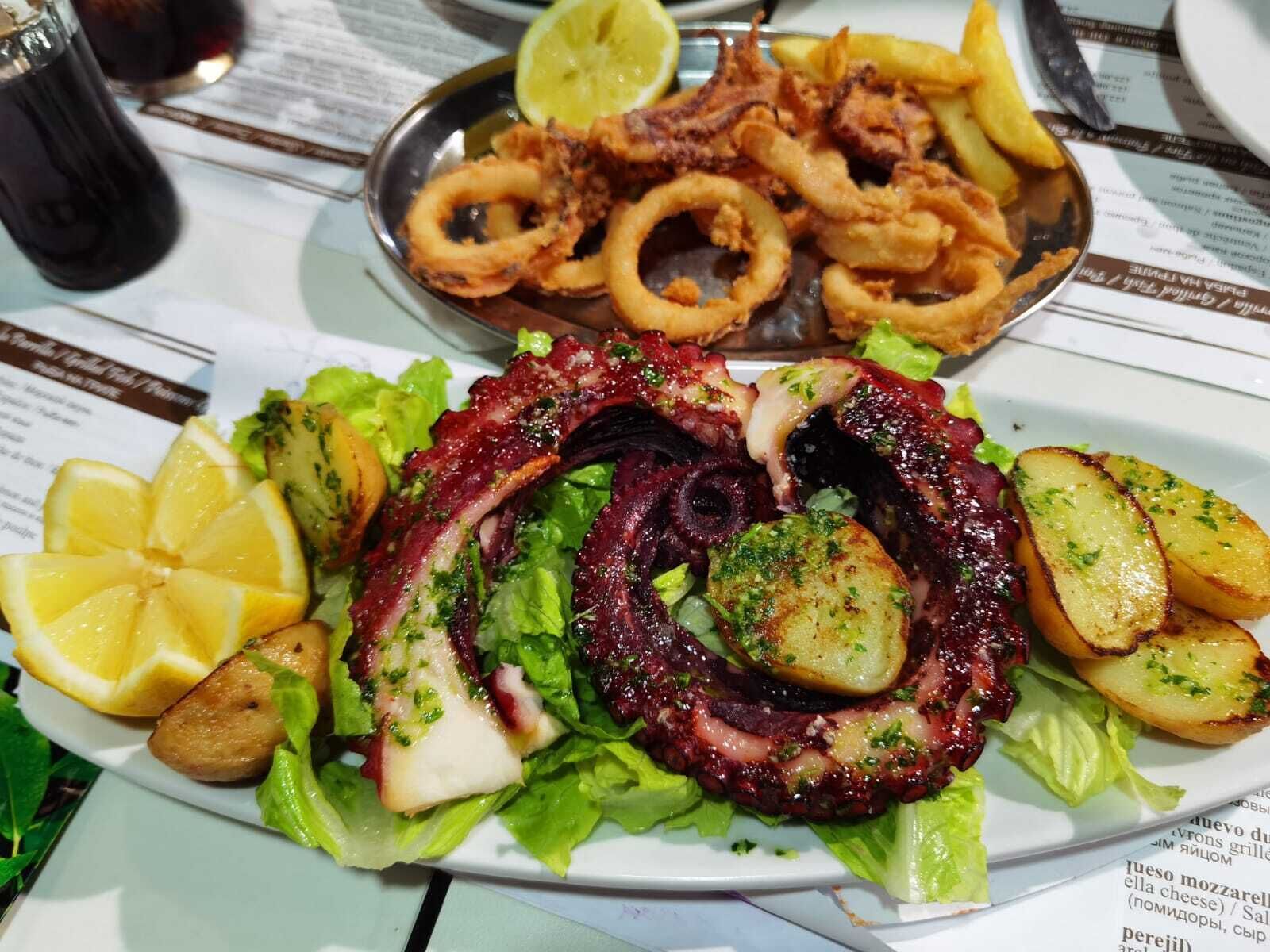 A plate of octopus salad with potatoes and lemon slices.