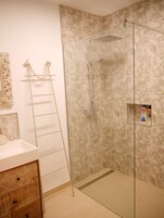 A bathroom with a shower, a sink, a mirror, and a wooden cabinet.
