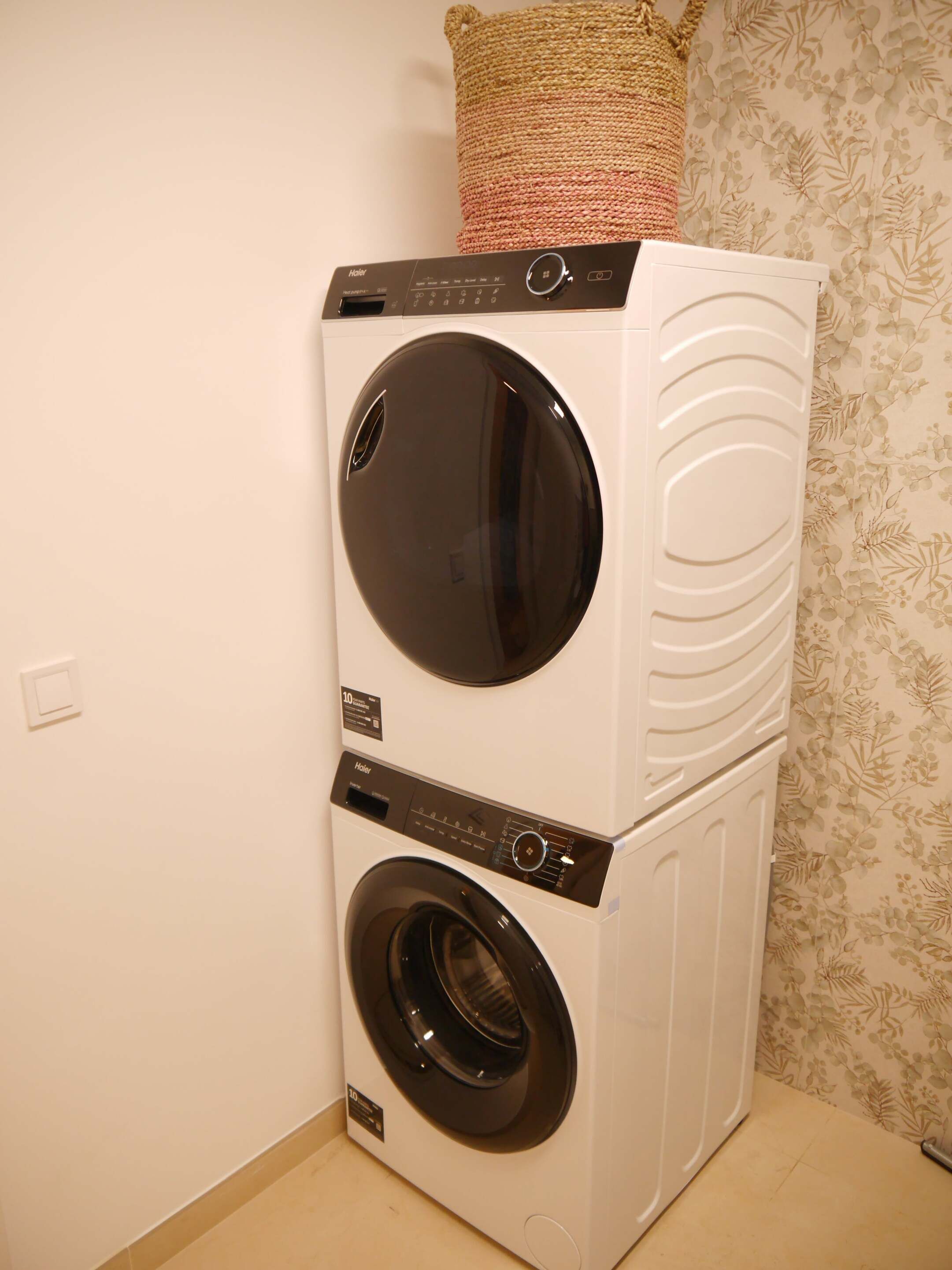 Lavadora y secadora apiladas con panel de control, un enchufe y un cojín decorativo encima.