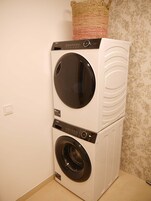 A stacked washer and dryer unit with a control panel, a power outlet, and a decorative pillow on top.