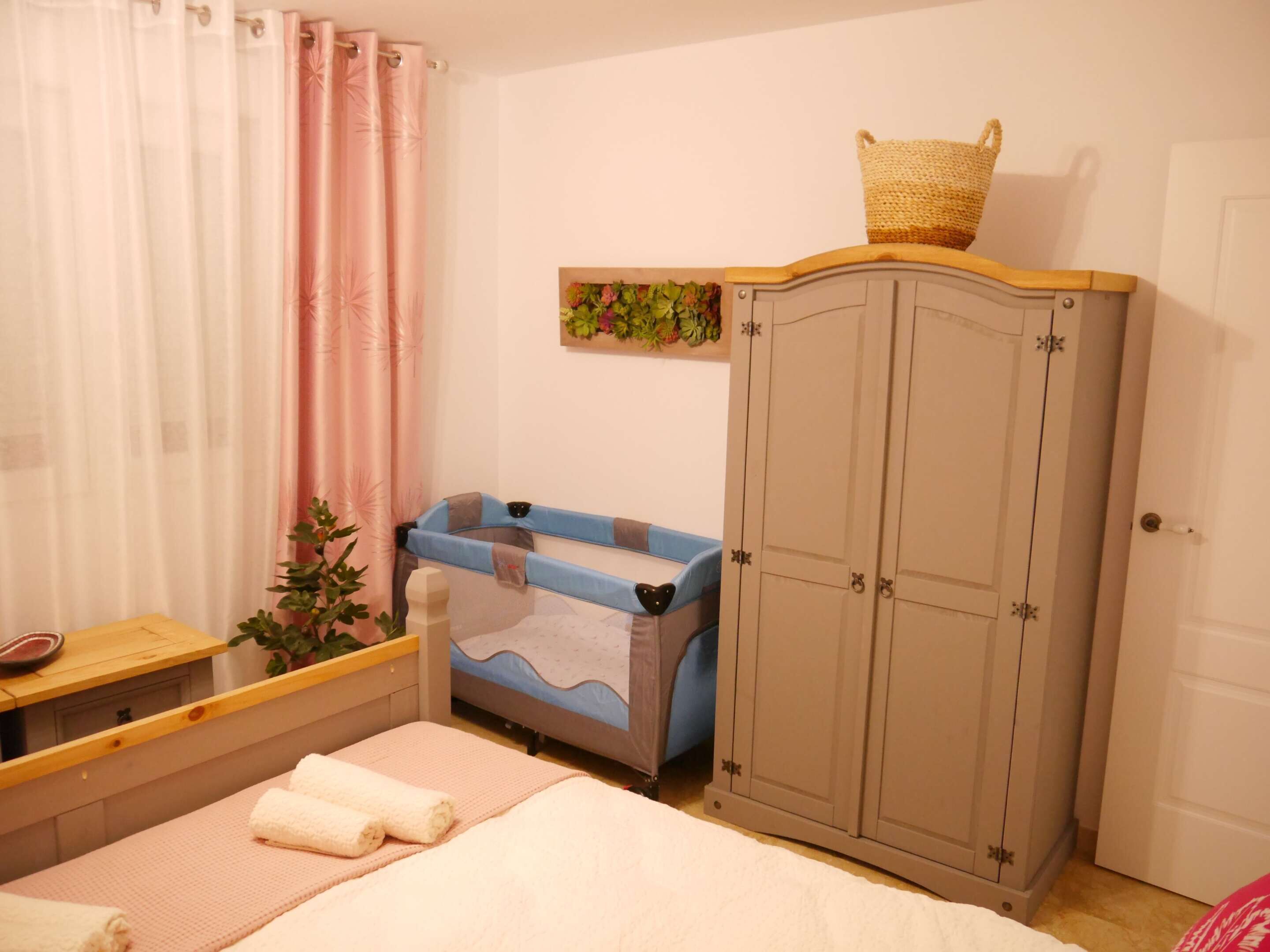 Ein Schlafzimmer mit einem Bett, einem Nachttisch aus Holz, einer blauen Badewanne, einem Kleiderschrank und einem kleinen Regal mit einem Korb.