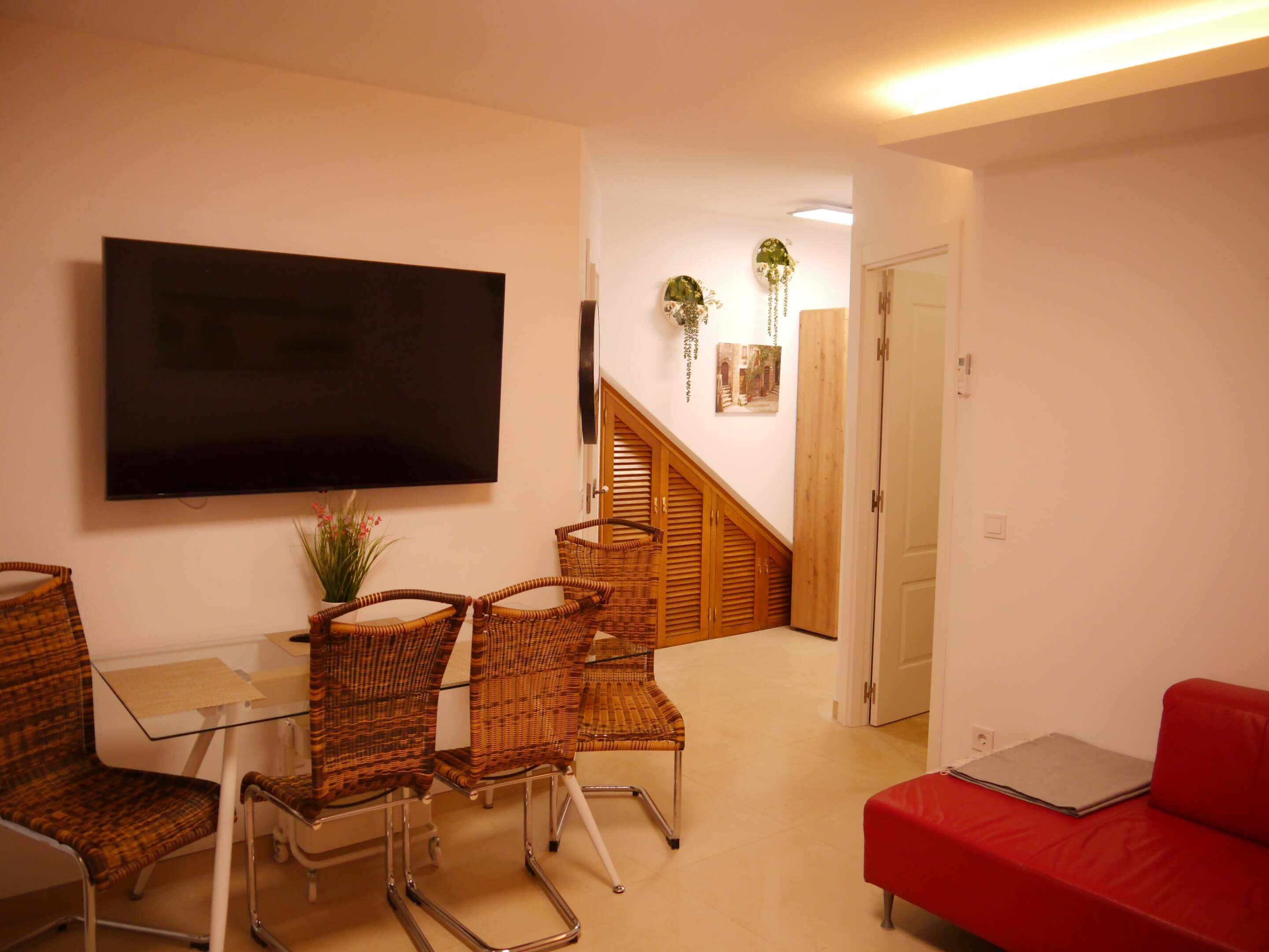 Un salon avec un téléviseur, des fauteuils en osier, un canapé rouge et un escalier.