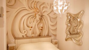 A bedroom with a large bed, a decorative headboard, a bedside table, and a wall-mounted mirror. - Casa Gibraltar (Estepona)