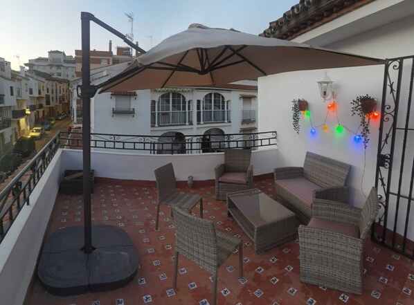 A balcony with wicker furniture, a table, and a large umbrella. - Casa Gibraltar (Estepona)