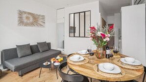 A modern living room with a grey sofa, a dining table set for four, and a vase of flowers.