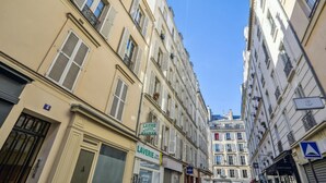 A narrow street with buildings on either side, featuring storefronts with signs for a laundry service and a hotel.