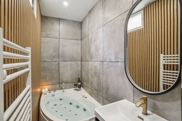 Une salle de bain moderne avec une baignoire sur pieds, un lavabo blanc avec un robinet doré et un grand miroir avec un cadre en bois.