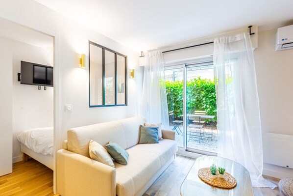 A modern living room with a sofa, a TV mounted on the wall, and a sliding glass door leading to an outdoor area.