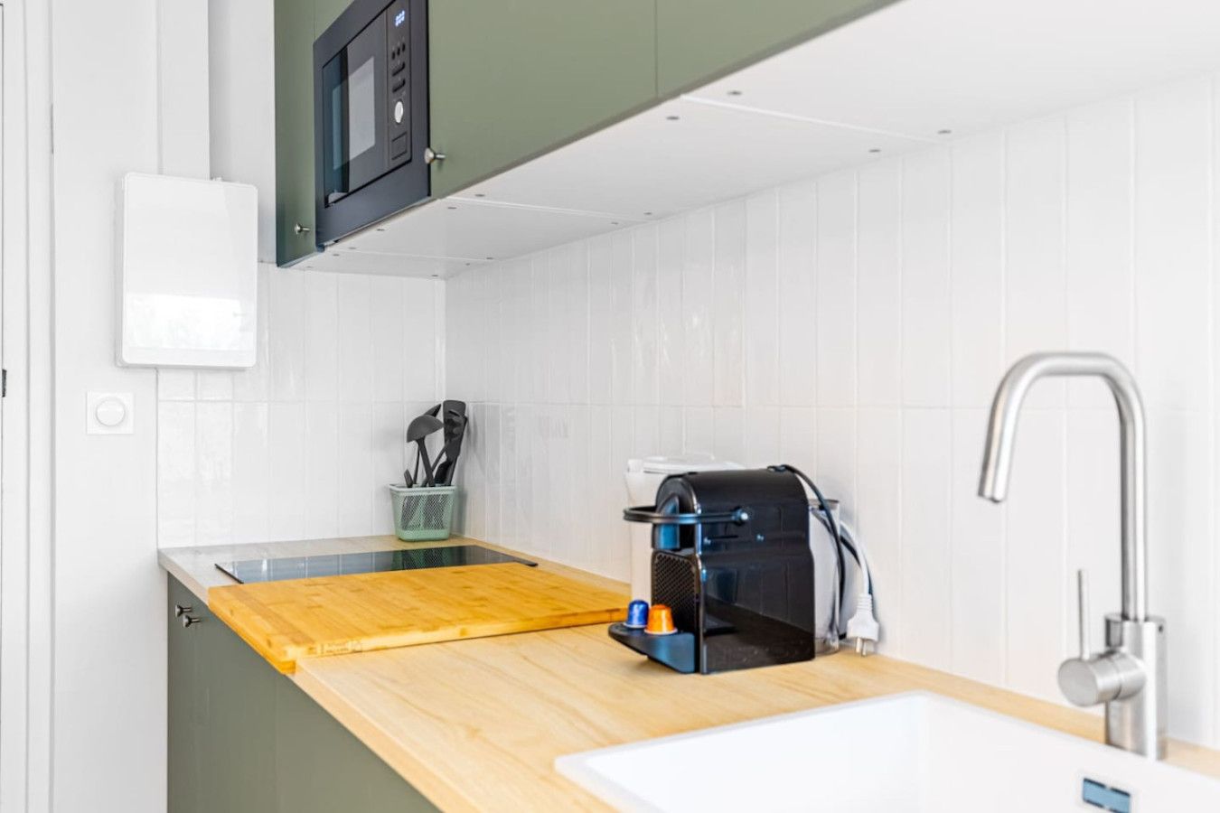 Uma cozinha compacta com bancada de madeira, micro-ondas embutido, máquina de café e uma torneira moderna.