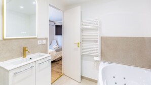 Un baño moderno con bañera, tocador con grifo dorado y un espejo grande.