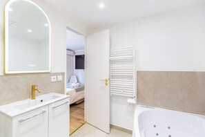 A modern bathroom with a bathtub, a vanity with a gold faucet, and a large mirror.