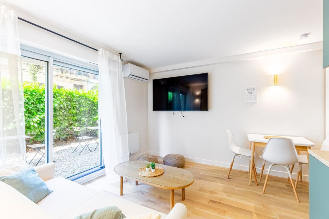 A modern living room with a large TV, a dining area, and a sliding glass door leading to a garden.