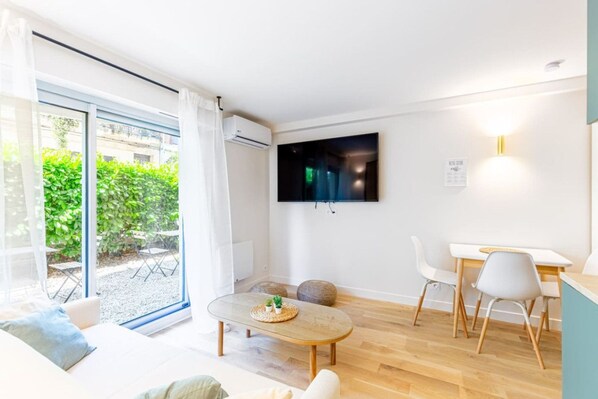 Una sala de estar moderna con un televisor grande, un comedor y un ventanal corredizo que da a un jardín.