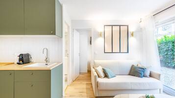 A modern kitchen with a sink, a coffee machine, and a green cabinet. There is a white sofa with cushions and a small table with plants.