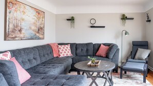 Un salon moderne avec un canapé d’angle, une table basse ronde et un lampadaire.