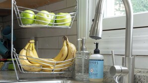 Un évier de cuisine avec un panier de fruits contenant des bananes et des pommes, un distributeur de savon et un robinet.