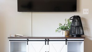 Un salon doté d’un téléviseur à écran plat fixé au mur, d’un meuble de rangement blanc avec des étagères, d’un canapé gris et d’une plante posée sur le meuble.