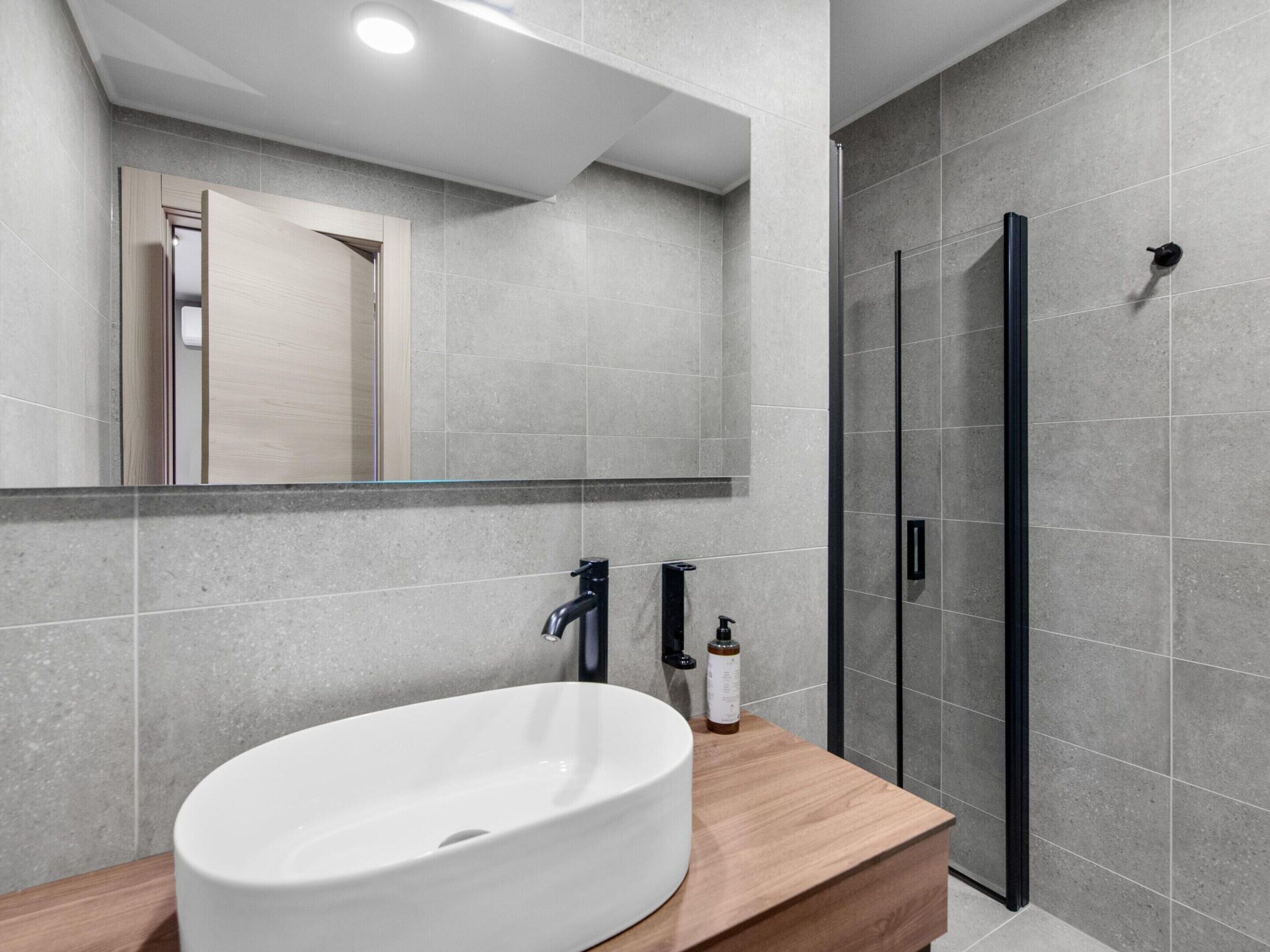 Une salle de bain moderne avec un grand lavabo blanc, un miroir et une douche à parois de verre.