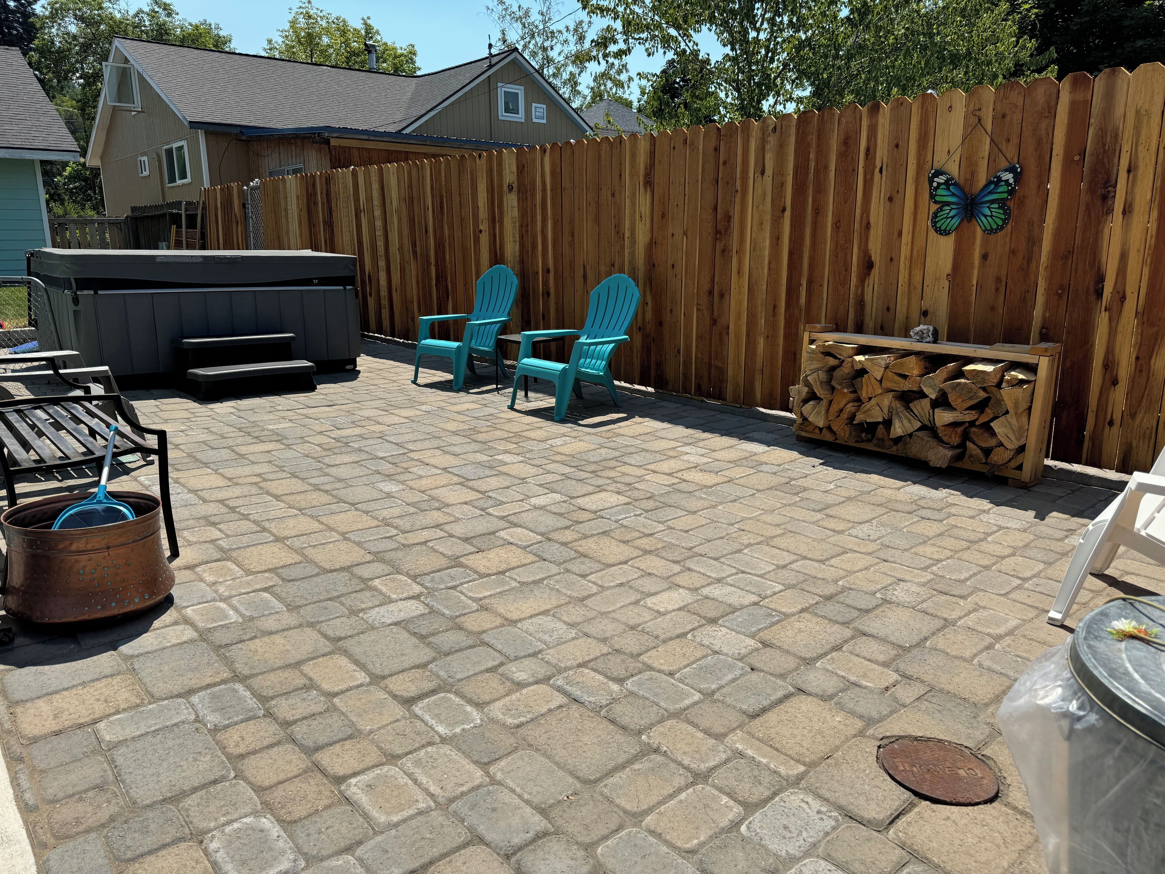 A backyard patio with a wooden fence, a grill, and a stack of firewood.