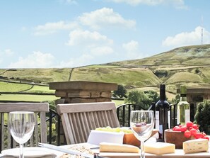 A table set outdoors with a view of rolling hills, a wine bottle, and cheese. - Mount View - UK48425 (Holmfirth)