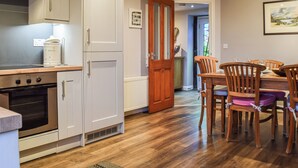 Une cuisine avec des meubles blancs, un fourneau et un coin repas comprenant des chaises et une table en bois.