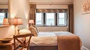 Une chambre à coucher avec un lit, des lampes de chevet, une chaise, une table et une fenêtre donnant sur un beau paysage.