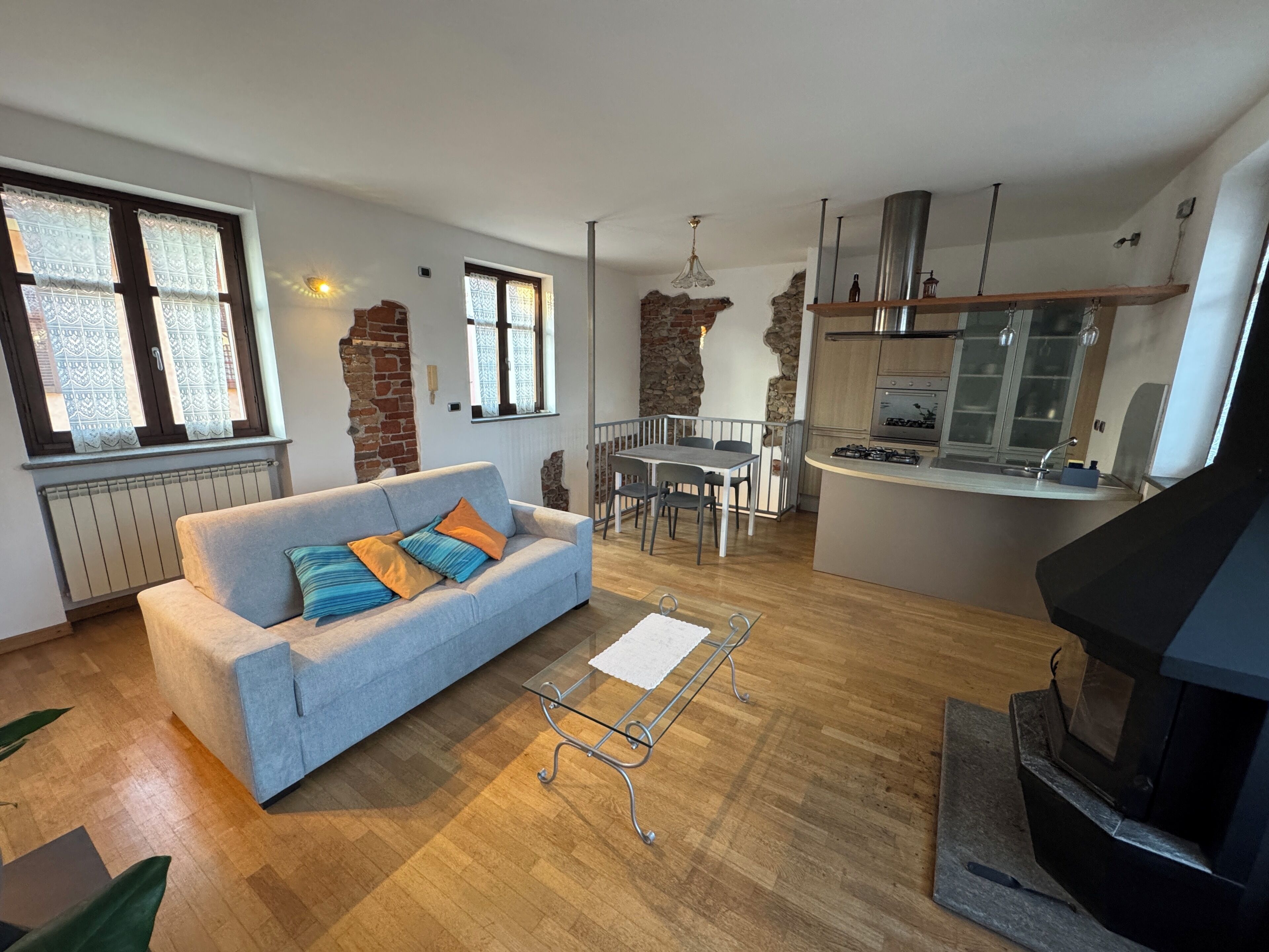 A modern living room with a grey sofa, a dining table, and a kitchen area with a stove and cabinets.