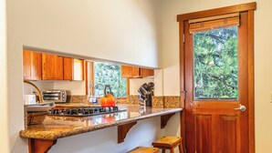 Una cocina con armarios de madera, encimera de granito, estufa y ventana con vista a árboles.
