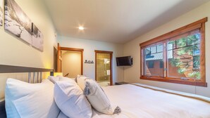 Un dormitorio con una cama grande, un televisor montado en la pared y una ventana que da a vistas de vegetación.