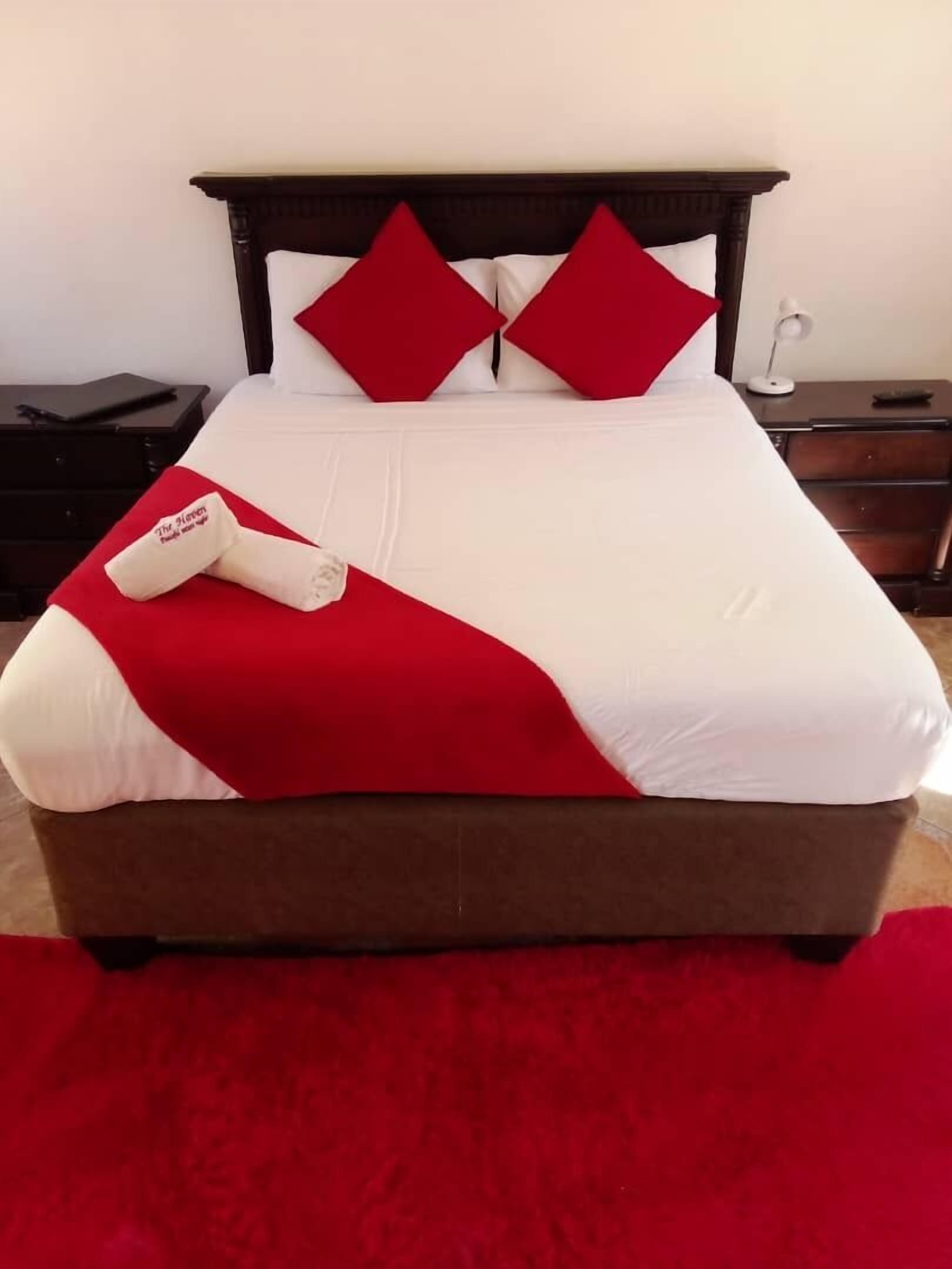 Una cama bien hecha con una colcha roja y blanca, dos almohadas rojas y una almohada blanca con un logotipo.