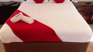 Una cama bien hecha con una colcha roja y blanca, dos almohadas rojas y una almohada blanca con un logotipo.