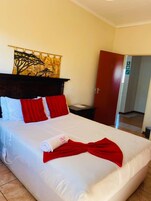 Una cama bien hecha con ropa de cama blanca y roja, un cabecero de madera, una puerta roja y un tapiz de un árbol en la pared.
